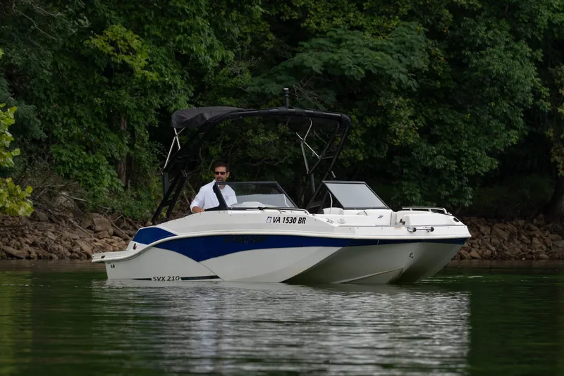 The Image of 2023 Starcraft SVX 210 IO boat on a calm lake with lush green trees. - 0