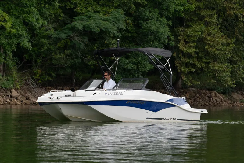 Slide: The Image of 2023 Starcraft SVX 210 IO boat cruising on a calm lake near a forested shoreline. - 2