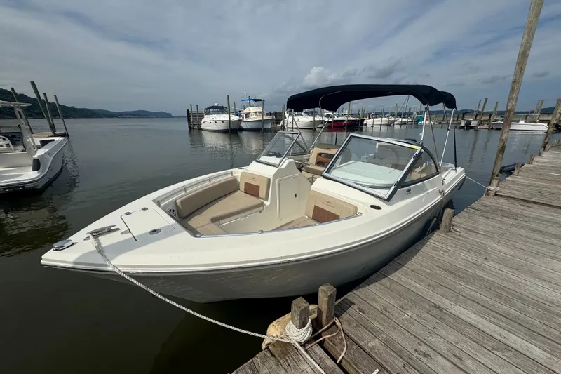 Slide: The Image of 2024 Cobia 220 Dual Console boat docked at a marina under a cloudy sky. - 2