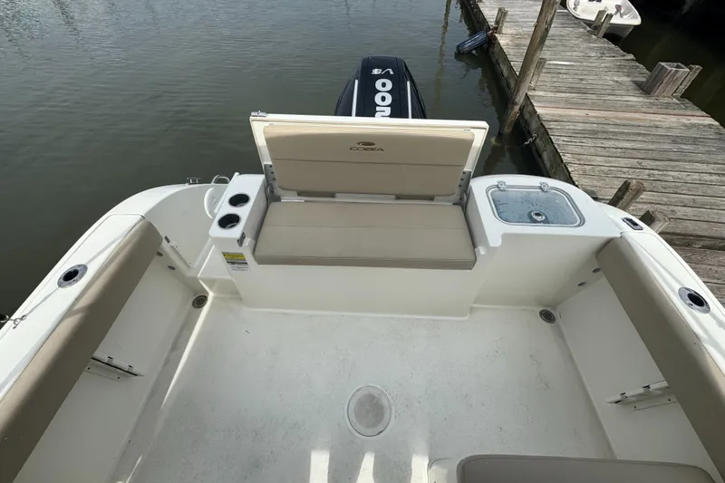 Slide: The Image of 2024 Cobia 220 Dual Console boat interior with seating and storage, docked by wooden pier. - 7