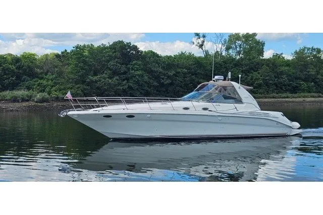 The Image of 1997 Sea Ray Sundancer 400 yacht cruising on a calm river with lush green trees. - 0