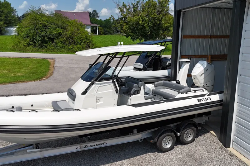 The Image of 2027 Brig Eagle 8 boat on trailer, parked near a garage, with lush greenery background. - 8