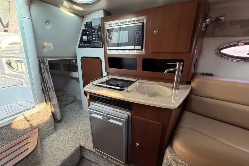 Slide: The Image of 2020 Crownline 264 CR boat interior with kitchenette, featuring sink, stove, and microwave. - 19