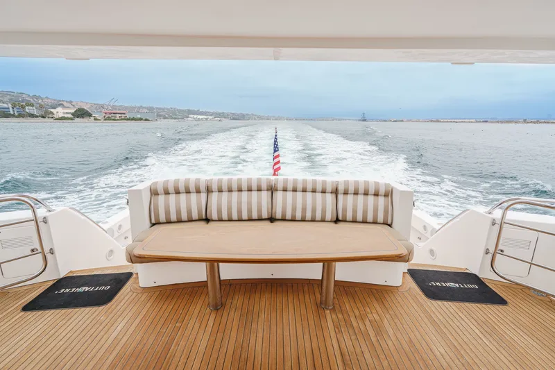 Slide: The Image of The image shows the stern of a 2005 West Bay 80 CPMY yacht with a sleek wooden table and striped cushions. The sea is visible in the background. - 38