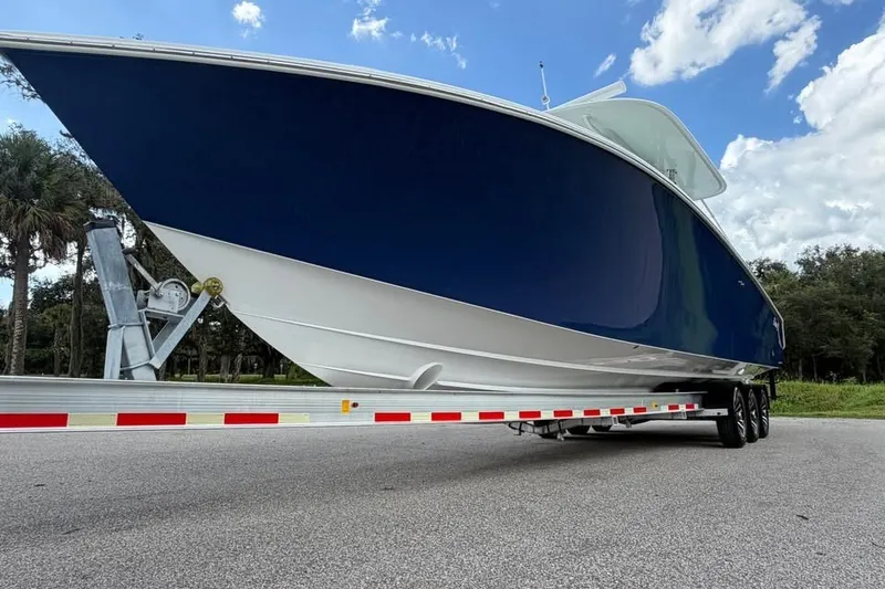 Slide: The Image of 2012 Bahama 37 boat on trailer, blue hull, parked on road under cloudy sky. - 6