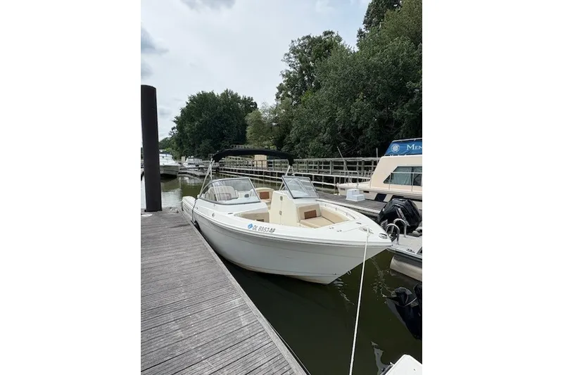 Slide: The Image of 2024 Cobia 220 Dual Console boat docked at a marina, surrounded by trees. - 3