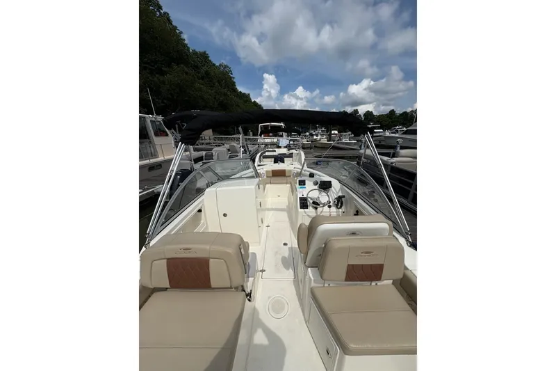 Slide: The Image of 2024 Cobia 220 Dual Console boat with beige seating, docked under a cloudy sky. - 6