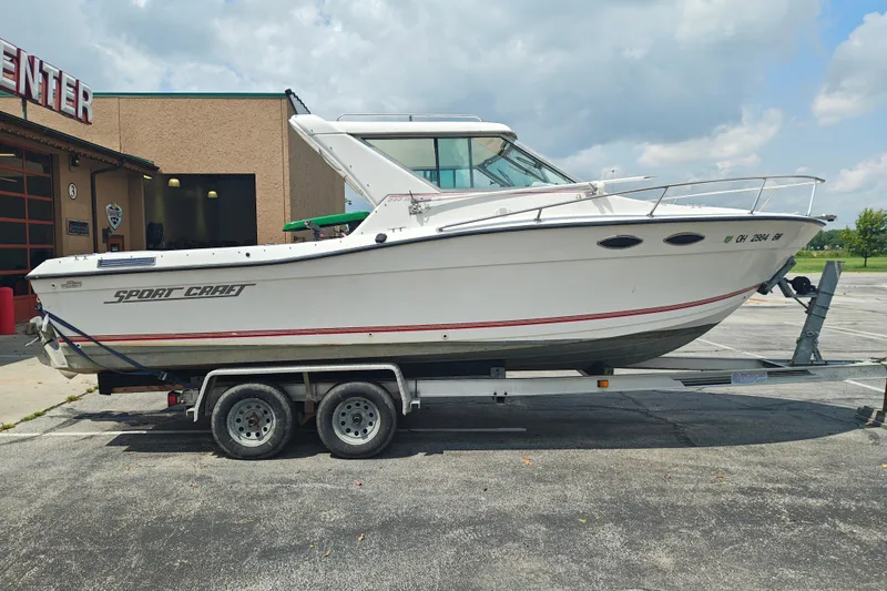 The Image of 1996 SportsCraft 232HT boat on trailer, parked outside a building under a cloudy sky. - 1