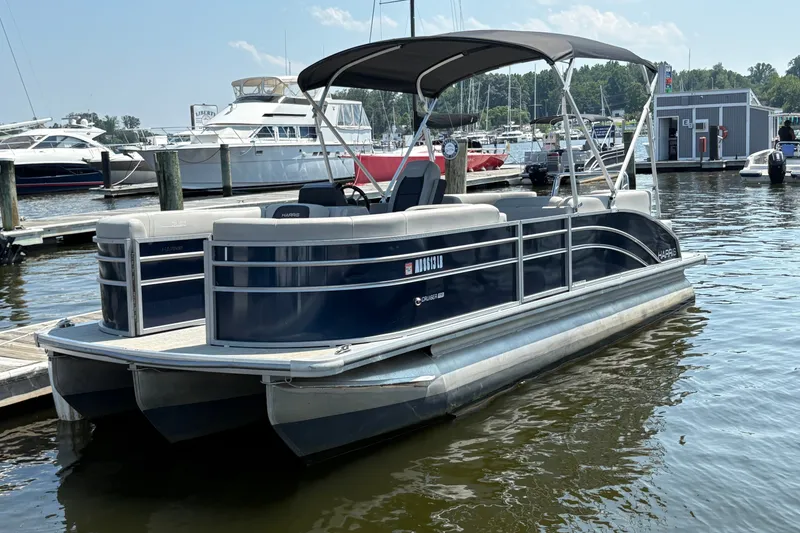 The Image of 2024 Harris Cruiser 230 pontoon boat docked at a marina, featuring sleek design and canopy. - 1