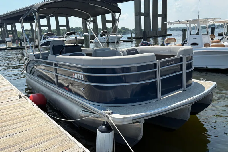 Slide: The Image of 2024 Harris Cruiser 230 pontoon boat docked at marina with bridge in background. - 2