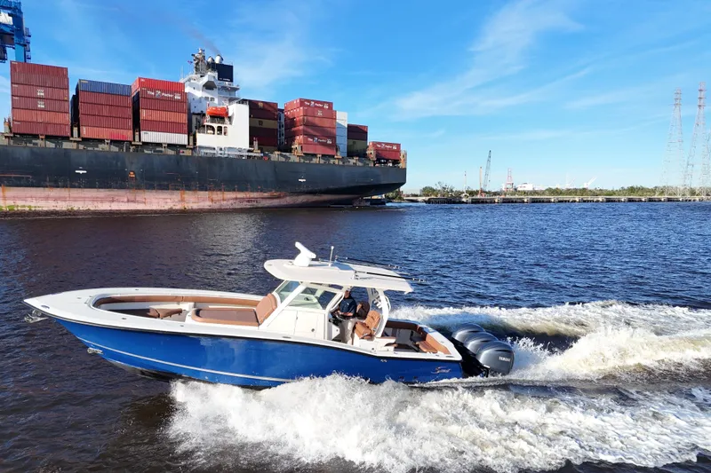 Slide: The Image of 2017 Scout 350 LXF boat cruising near a large cargo ship on a sunny day. - 25