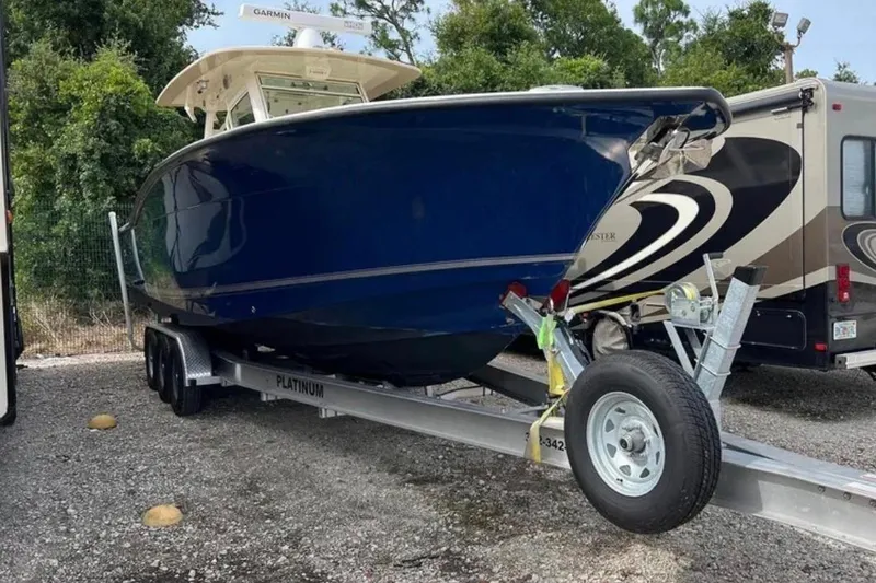 Slide: The Image of 2017 Scout 350 LXF boat on trailer, parked beside RV, surrounded by trees. - 79