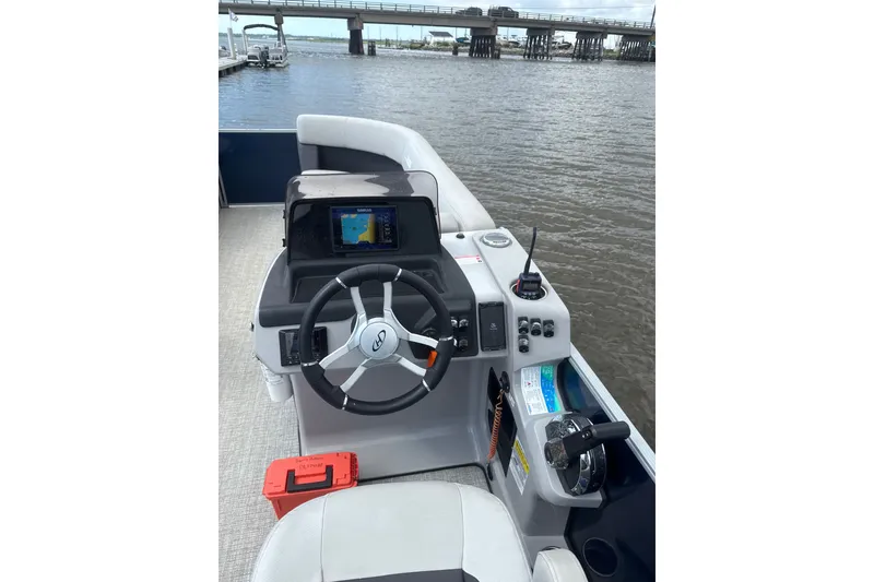 Slide: The Image of 2024 Harris Cruiser 230 boat helm with steering wheel and navigation system on a river. - 6