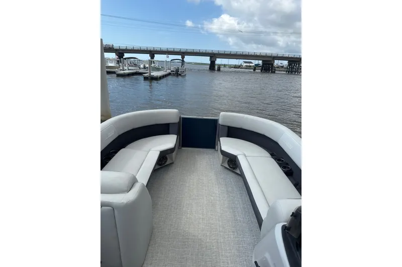 Slide: The Image of 2024 Harris Cruiser 230 pontoon boat interior with plush seating, docked near a bridge. - 5