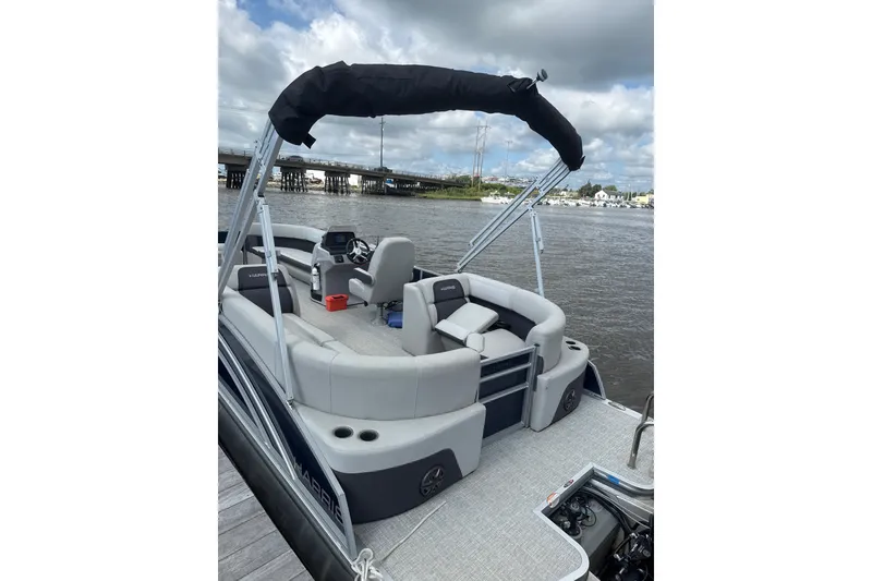 Slide: The Image of 2024 Harris Cruiser 230 pontoon boat with spacious seating and canopy on a calm river. - 3