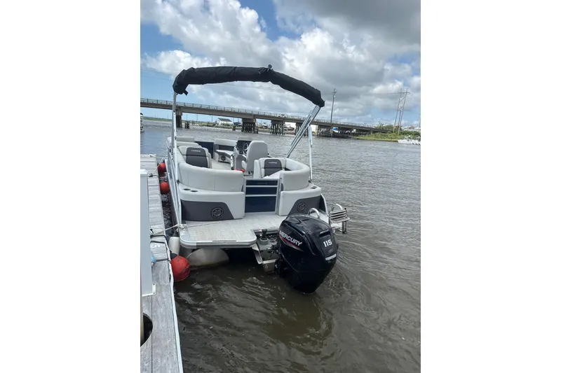 Slide: The Image of 2024 Harris Cruiser 230 pontoon boat docked on a calm river under cloudy skies. - 2