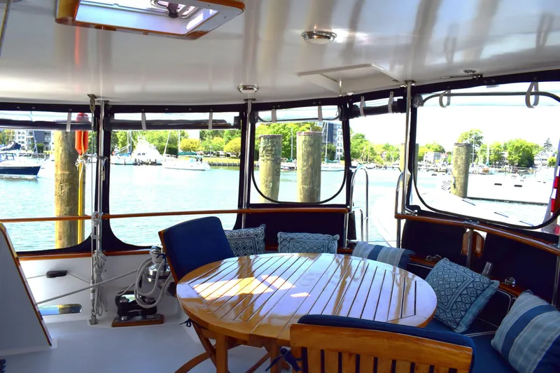 Slide: The Image of 1980 Cheoy Lee 52 Motorsailer cockpit with wooden table, cushioned seating, and marina view. - 36