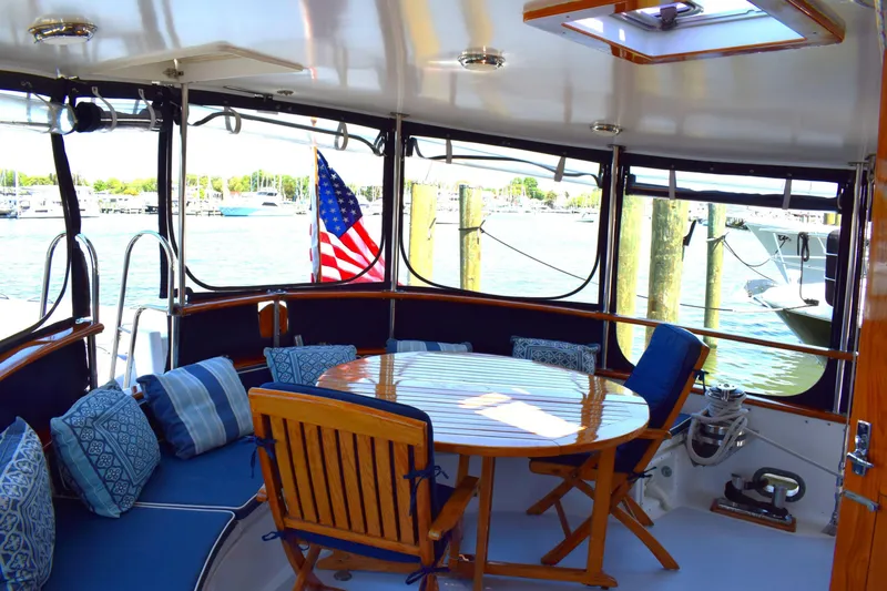 Slide: The Image of 1980 Cheoy Lee 52 Motorsailer cockpit with wooden table, cushioned seating, and marina view. - 35