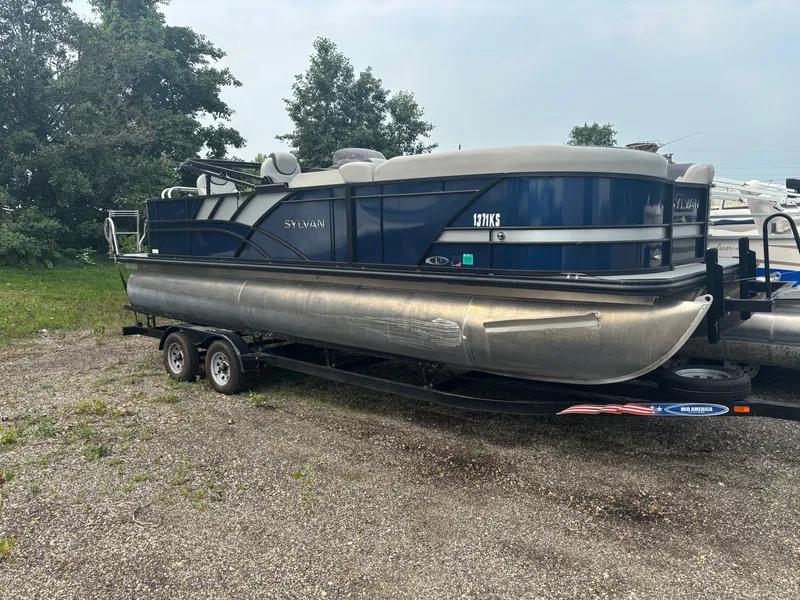 The Image of A 2021 Sylvan L3PF TRITOON on a trailer, surrounded by trees and other boats. - 0