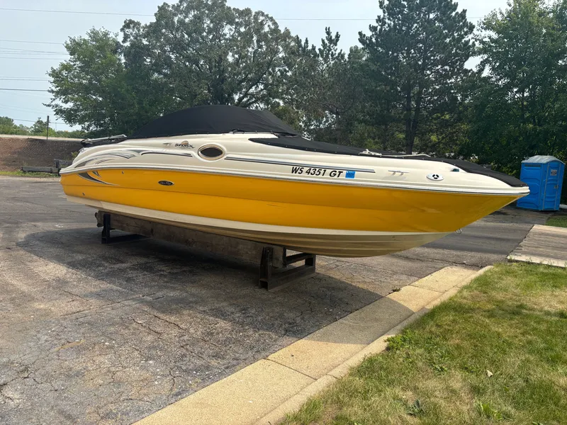 The Image of A yellow 2005 Sea Ray 240 Sundeck is parked on a lot, surrounded by trees. - 0