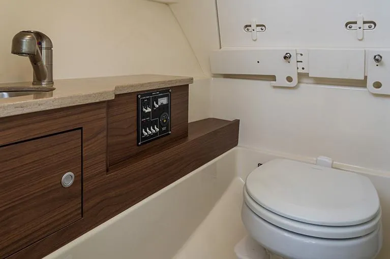 Slide: The Image of Manufacturer Provided Image: 2026 Boston Whaler 280 Vantage boat interior with compact bathroom and wooden cabinetry. - 17