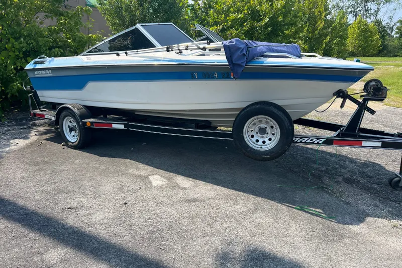 The Image of 1990 Armada Luxura 170 SZ boat on trailer, parked outdoors, surrounded by greenery. - 0