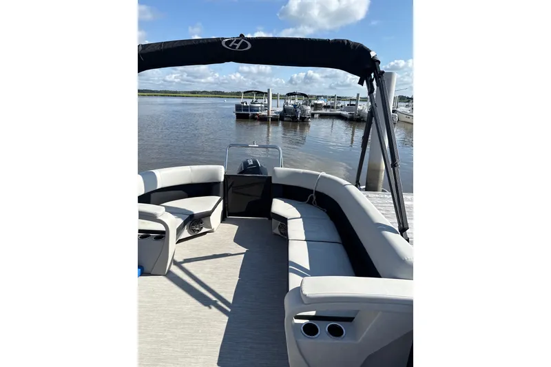 Slide: The Image of 2024 Harris Breeze 230 pontoon boat with spacious seating, docked by a serene waterfront. - 6