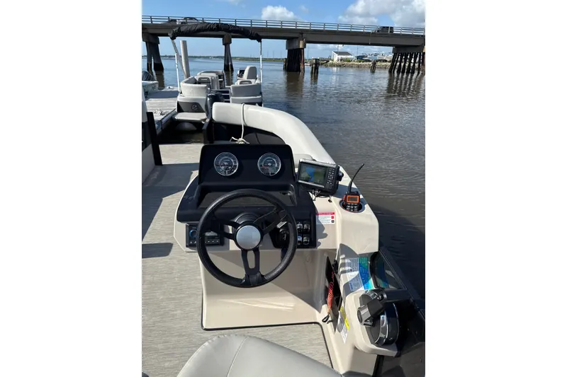 Slide: The Image of 2024 Harris Breeze 230 boat dashboard with steering wheel and navigation equipment, docked by a bridge. - 5