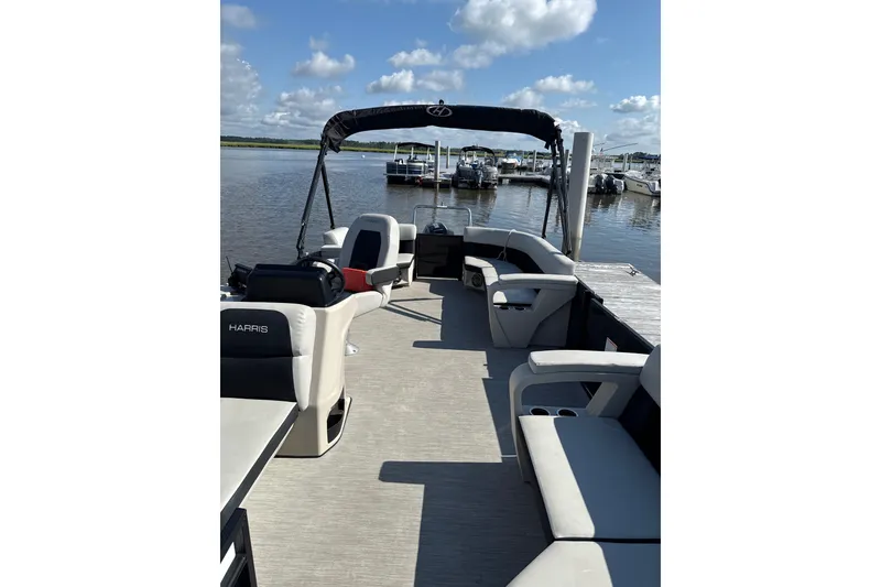 Slide: The Image of 2024 Harris Breeze 230 pontoon boat docked, featuring spacious seating and a scenic waterfront view. - 8