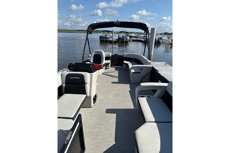 Slide: The Image of 2024 Harris Breeze 230 pontoon boat with spacious seating, docked by a serene lake. - 2