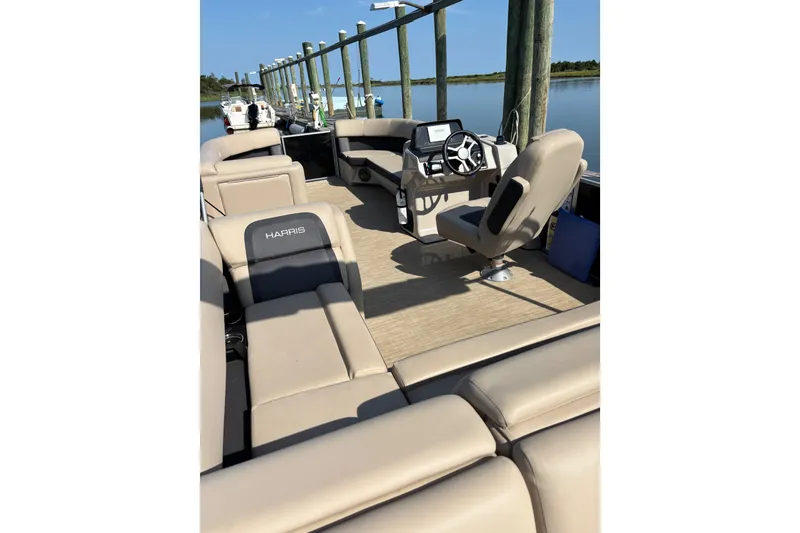 Slide: The Image of 2024 Harris Cruiser 230 pontoon boat interior with beige seating and steering console. - 2