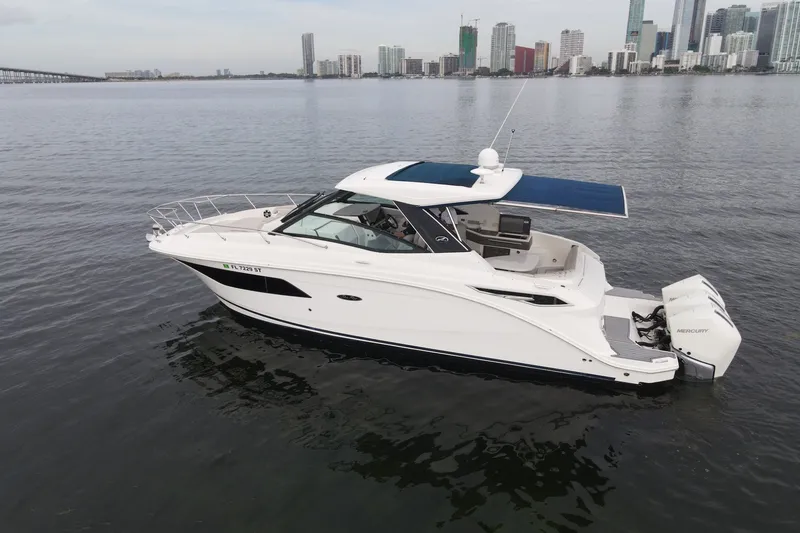 Slide: The Image of 2020 Sea Ray Sundancer 320 Coupe Outboard cruising on calm waters near city skyline. - 1