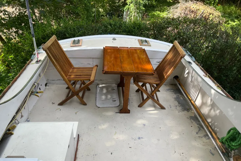 Slide: The Image of Wooden chairs and table on a 1970 Dyer 29 boat deck, surrounded by greenery. - 23
