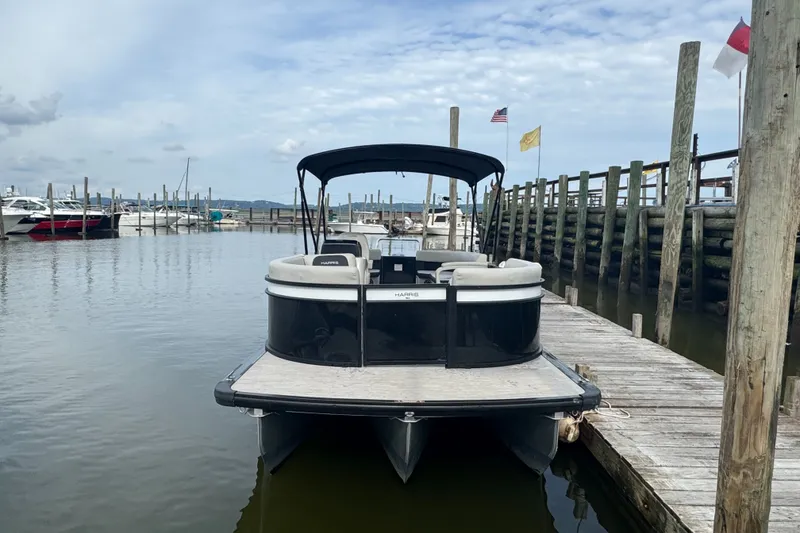 Slide: The Image of 2024 Harris Breeze 230 pontoon boat docked at a marina under a cloudy sky. - 1