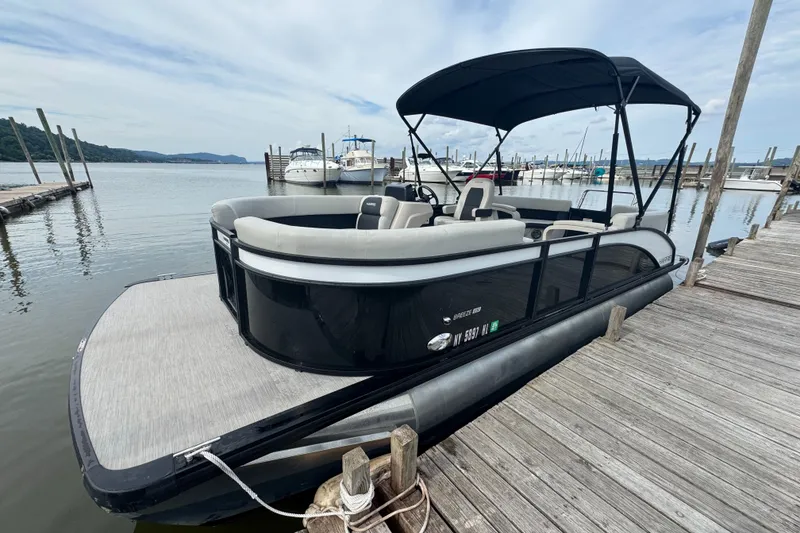 The Image of 2024 Harris Breeze 230 pontoon boat docked at a marina, featuring sleek design and spacious seating. - 2