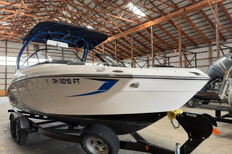 The Image of 2018 Yamaha Boats 242X E-Series in a warehouse, on a trailer, with blue accents. - 0