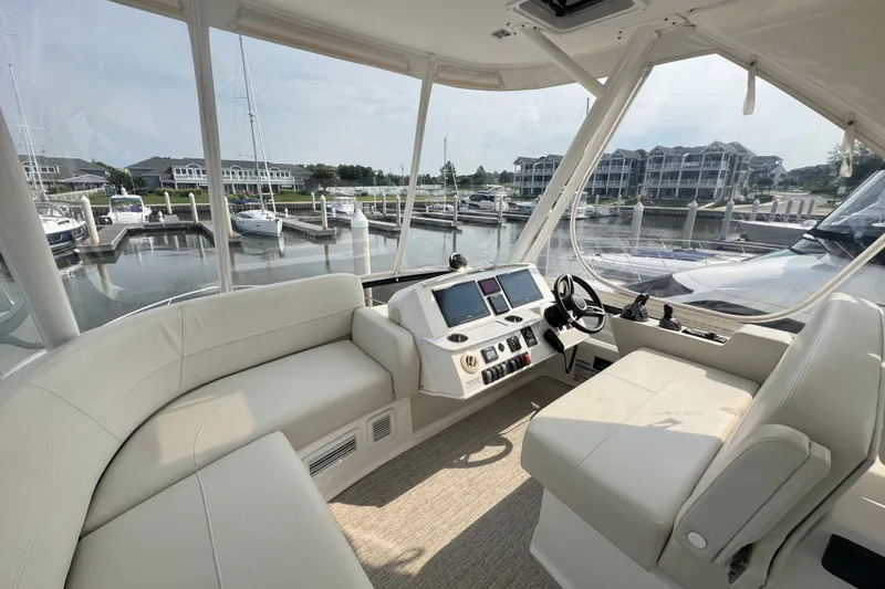 Slide: The Image of 2021 Tiara Yachts F44 Flybridge interior with helm, seating, and marina view. - 38