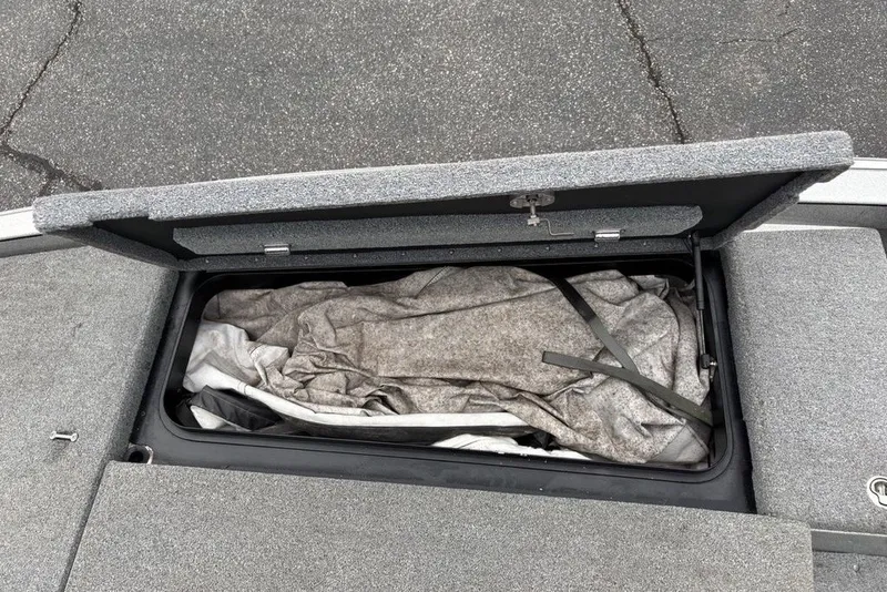 Slide: The Image of Open storage compartment in 2018 Skeeter FX21 boat, containing folded tarp and straps. - 17