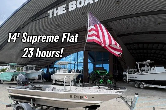 The Image of 14-foot Supreme Flat boat with American flag, displayed outside dealership, 2023 model. - 0