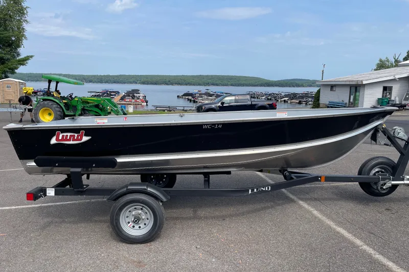 The Image of 2027 Lund WC 14 boat on trailer near a lake with docked boats. - 0