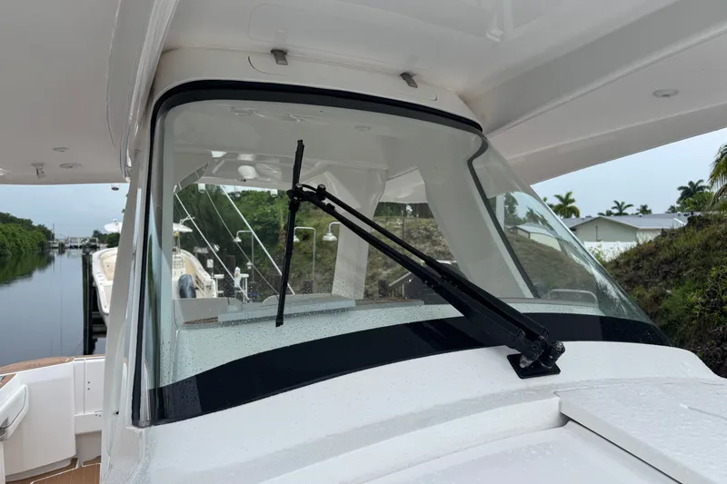 Slide: The Image of 2022 Intrepid 345 Nomad SE boat windshield with wiper, docked near lush greenery. - 14
