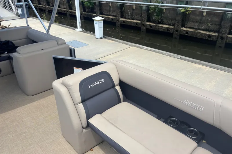 Slide: The Image of 2024 Harris Cruiser 230 boat interior with beige seating and cup holders at a dock. - 8
