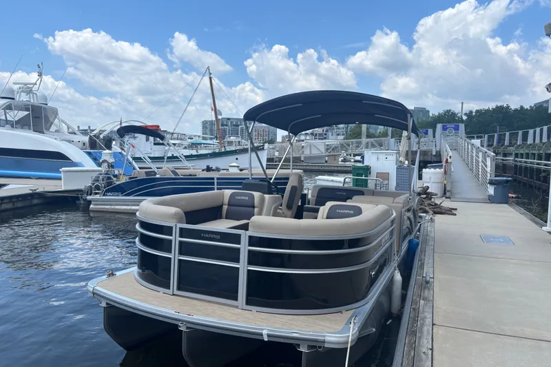 Slide: The Image of 2024 Harris Cruiser 230 pontoon boat docked at a marina under a blue sky. - 2