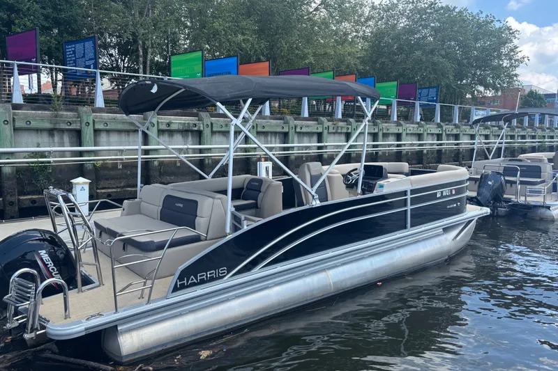Slide: The Image of 2024 Harris Cruiser 230 pontoon boat docked by a colorful waterfront. - 3