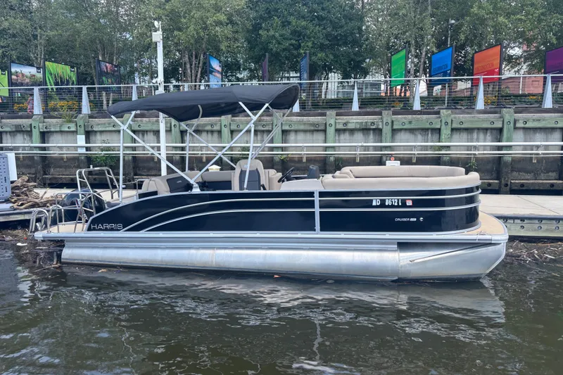 The Image of 2024 Harris Cruiser 230 pontoon boat docked by a scenic waterfront. - 1