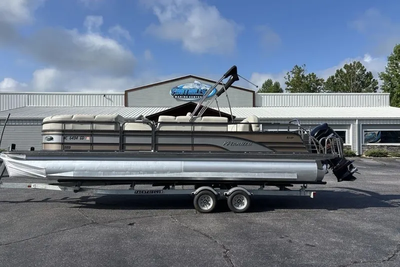 The Image of 2015 Manitou 25 SHP SES pontoon boat on trailer, parked outside a marine center. - 1