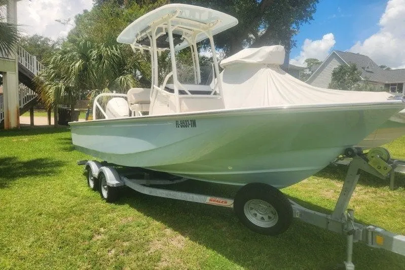 Slide: The Image of 2023 Boston Whaler 210 Montauk boat on trailer, parked on grass under a sunny sky. - 0