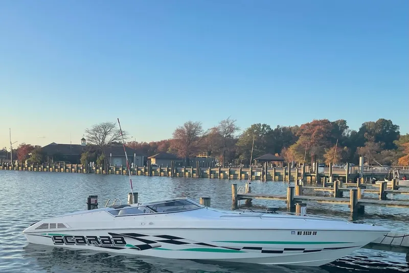 The Image of 2000 Wellcraft 29 Scarab boat docked on a serene lake with autumn trees. - 0