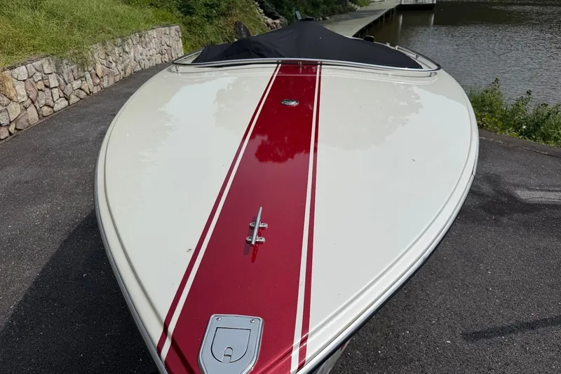 Slide: The Image of 1990 Donzi Sweet 16 boat with red stripe, parked near a stone wall by the water. - 3