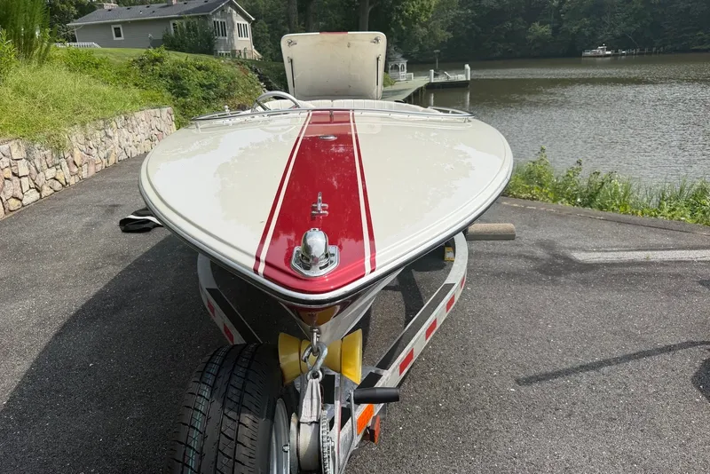 Slide: The Image of 1990 Donzi Sweet 16 boat with red stripe on trailer by a lakeside driveway. - 13